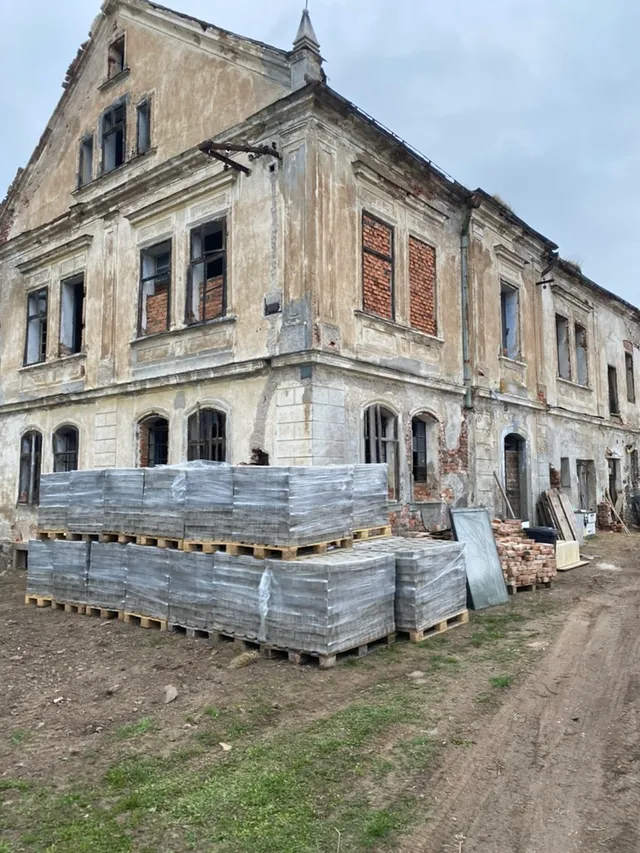 Palety dlažby složené u nároží zámečku. Mezi sutí najednou kus budoucího povrchu.