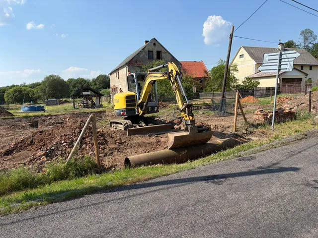 První verze provizorního vjezdu: roura přes příkop a bagr připravený na další práci.