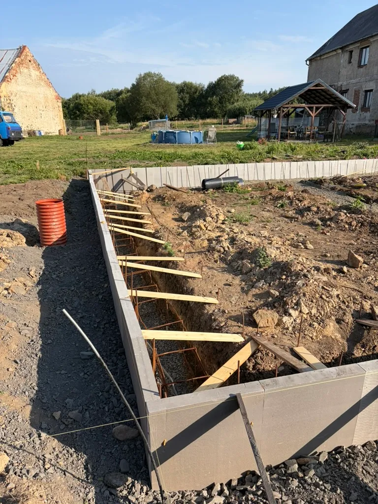 Před betonáží drží horní hranu XPS řada dřevěných vzpěr. Vnější strana je obsypaná kamenivem.