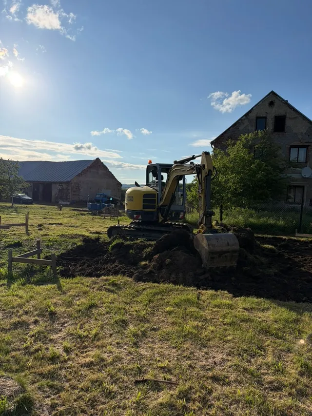Kolíky a jednoduché lavičky drží obrys, bagr pomalu stahuje vrchní vrstvu zeminy.