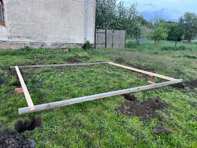 Pohled podél rámce ke vrátkům. V každém rohu jáma na patku, vedle hromádka vykopané hlíny.