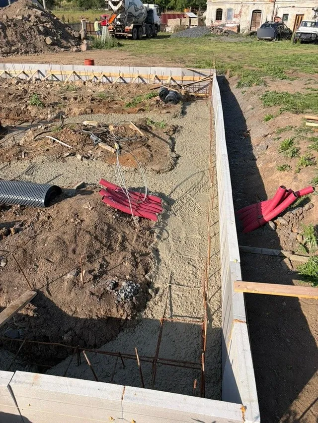 Čerstvý beton v pásech. U okraje je vidět XPS, vzpěry i chráničky připravené pro další práce.