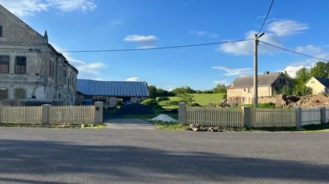 Hotový plot od silnice. Světlá laťová výplň lemuje pozemek, uprostřed vjezd, vpravo obytná část statku.