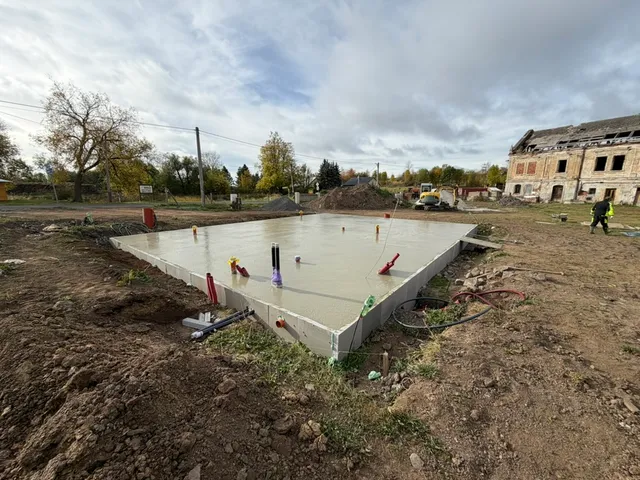 Čerstvě zabetonovaná základová deska s domíchávačem v pozadí.