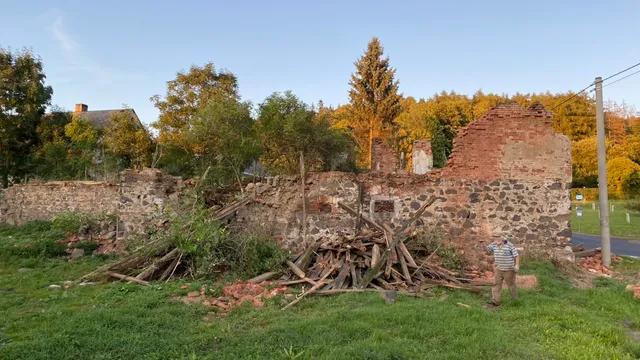 Hromada vytahaných trámů u kamenné zdi. Táta u ní dává představu o měřítku.