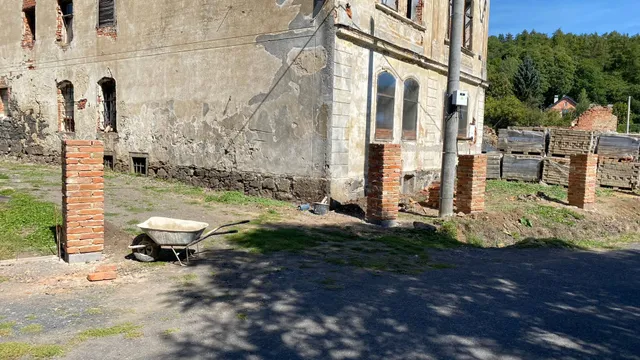 Sloupky podél zdi zámečku. Vzadu palety cihel připravené na další metry plotu.
