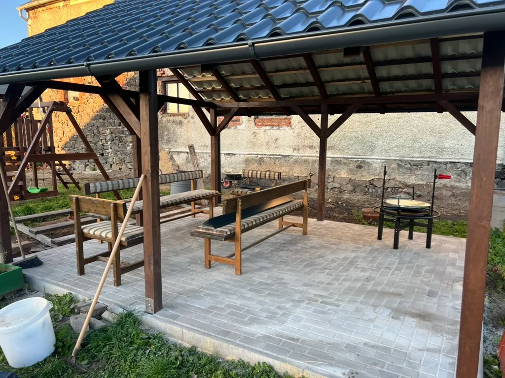 Pod hotovou střechou lavice, stůl a ohniště. Přesně tohle byl celou dobu cíl — kryté místo k posezení.